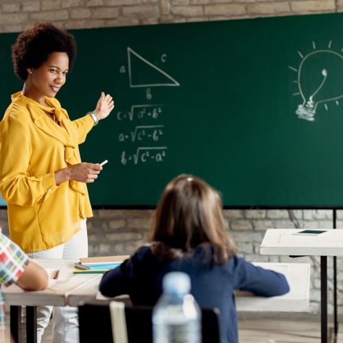 Happy black teacher teaching elementary students math in the cla Happy African American teacher talking to school children while explaining them mathematic on a class in the classroom.